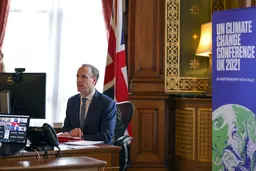 Man sitting on a desk in front of a computer, with the Union flag behind him