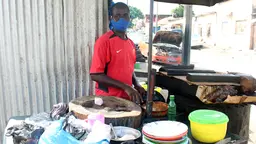 A mask-wearing man stands behind a food stall