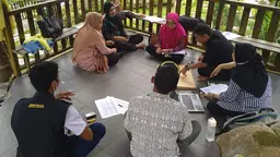 Men and women sit on the floor to talk with computers and paper in front of them 