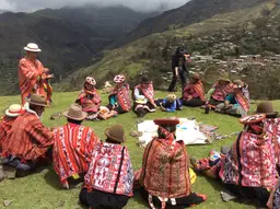 People wearing traditional clothing sit in a circle in a field.
