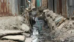 Sewage and water runs down the centre of a makeshift 'drain' surrounded by sandbags and wood