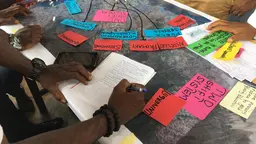 Table with coloured papers and someone writing on a notebook