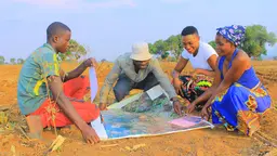Four people sit on the floor to look at a map on the ground.