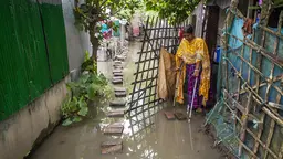 Woman waling with crutches steps outside a hut to a flooded road