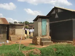 A small brick building with two steps leading to a corrugated iron door houses a pit latrine.