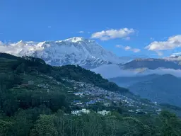 View of a mountain with a few houses. Snowed mountains in the background. 