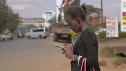 Woman wearing a blazer checks her mobile phone in the street.