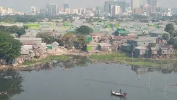 View of informal housing by a lake, with a boat in it. In the background modern buildings and skyscrapers