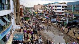 View of a busy street with clothes stalls and shops and people walking.