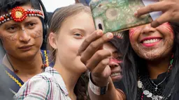 A close-up of a young girl, amid a crowd of people, looking at a mobile phone being held up for her