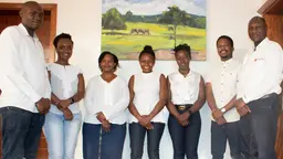 A group of men and woman stand for a group photograph in front of a painting.