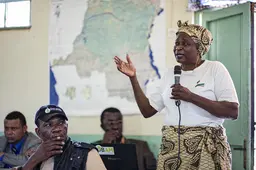 Woman speaking with a microphone to an audience of men.