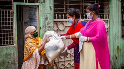 Two women wearing masks hand over a bag to another woman wearing a mask