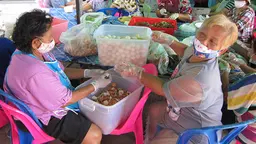 Two women wearing face masks are sitting at a table covered in boxes and bags of vegetables. Together they are preparing food.