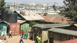 A busy African street scene, with industrial buildings in the background.