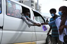A woman wearing a mask sprays a lqiuid on someone else's hands.