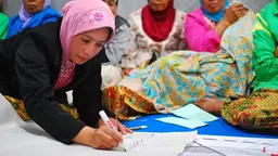 A woman writes on a poster. More women appear blurred in the background.
