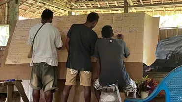 Three community members discussing and writing things down on a flip chart.