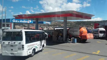A bus queues outside a petrol station at which a tanker is filling up with petrol 