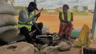 A man and woman sat down cooking with a charcoal cookstove.