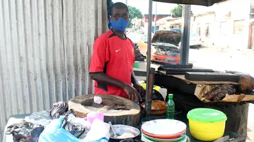 A mask-wearing man stands behind a food stall