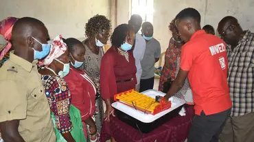 A group of men and women wearing masks stand around a device being demonstrated by a man.