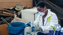 A woman wearing a mask pours chemicals into a bottle.