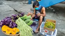 Man sits on the floor holding aubergines. In front, there's a table with vegetables.