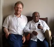 Two men sit on a coach alongside one another.