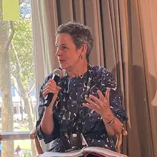 A woman seated in a panel speaks into a microphone.