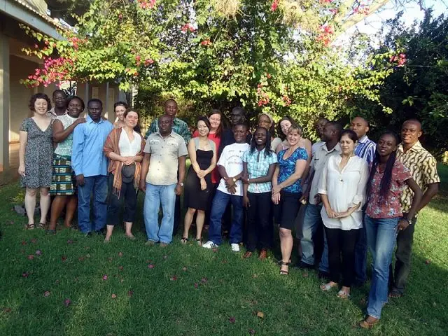 A group of men and women smile and pose for a photo outside with trees in the background.