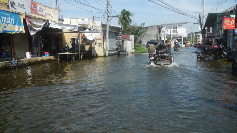 A vehicle driving down a flooded street in an urban area.