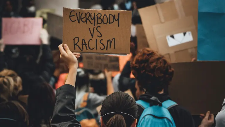 Woman in a demonstration holds a sign that reads "Everybody vs racism"
