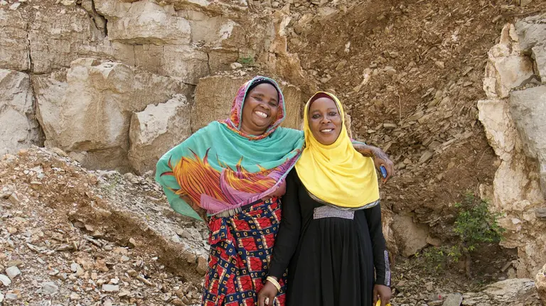 Two woman smile and pose for a photo in front of a quarry