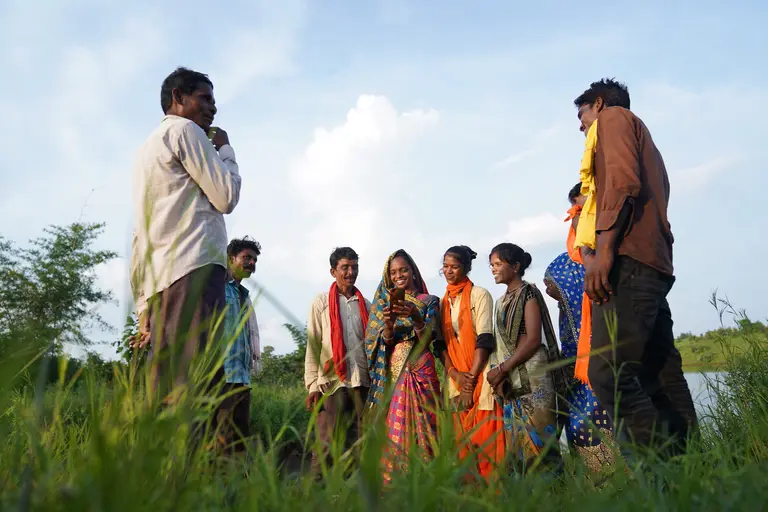 Smiling women and men standing in a field looking at a mobile phone