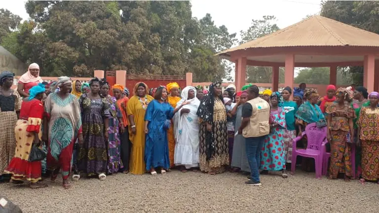 A large group of women stand outside in a line listening to a man who is addressing them.