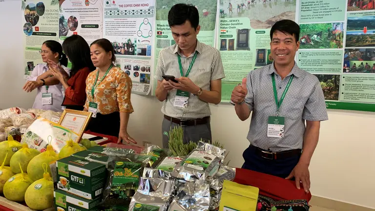 Men and women stand behind a stand with products. A man smiles at the camera