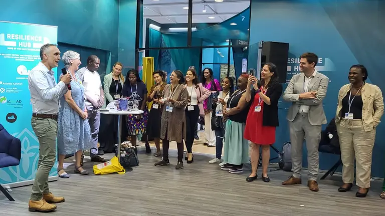 A groupo of people stand around a man speaking to the group.
