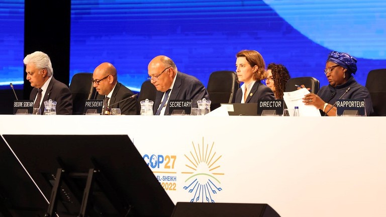 Five men and women wearing suits sit at a long table with microphones. The tables reads "COP27"