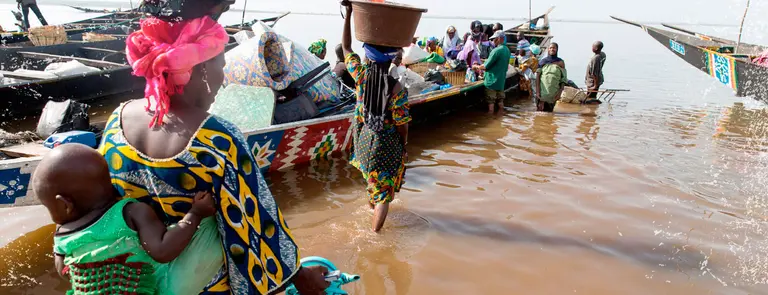 Women wade out to load a boat with cargo