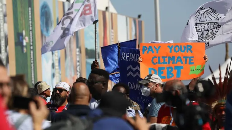 Mass of people walking with flags and posters. A sign reads "pay your climate debt"