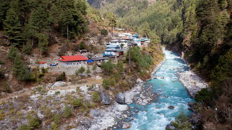 A small town sits beside a river with mountains in the background