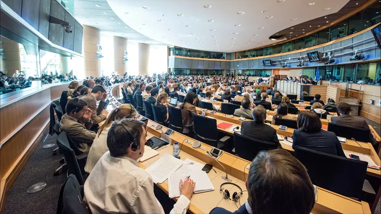 A group of people sitting at desks in a room facing a panel
