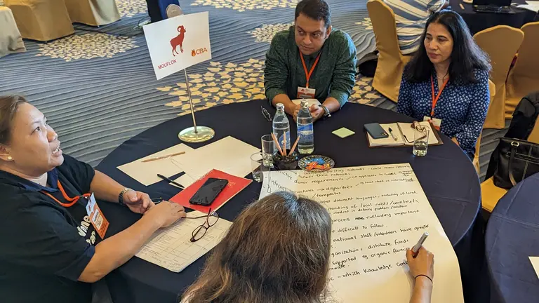 People sitting on a round table and writing notes on a poster.