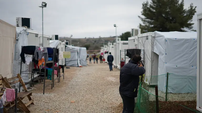 Man in black jacket walking among temporary tents and shelters.