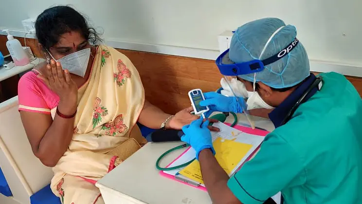 A doctor wearing protective clothing treats a woman patient over a desk.