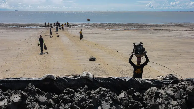 A group of people on a beach adding large lumps of clay to an embankment in the foreground.