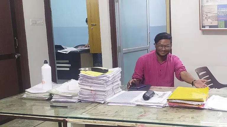 A man sits a table with lots of stacked paperwork.