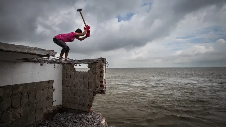 Man standing on a house roof holds a hammer.