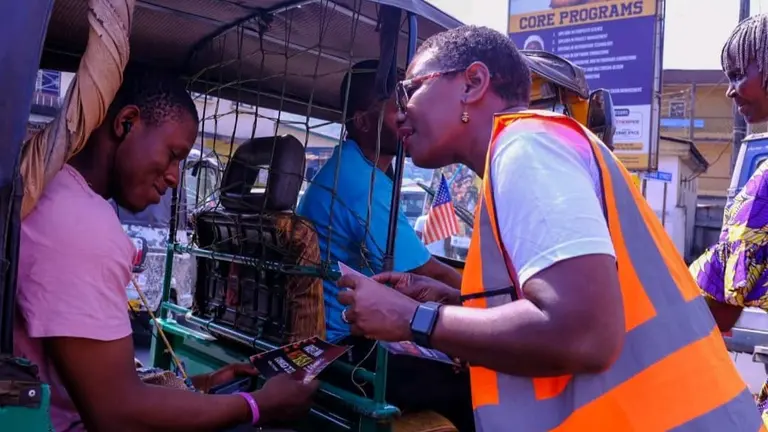 A woman in an orange vest speaks to another person in a vehicle.